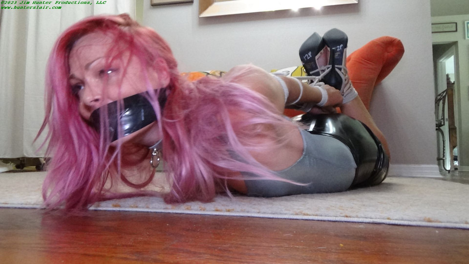Tight and shiny hogtied struggles on the carpet